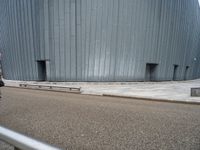 an empty road leading to a large building with a metal structure on one side and steps going up to the top