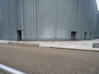 an empty road leading to a large building with a metal structure on one side and steps going up to the top