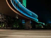 an illuminated pedestrian bridge is going over the street at night and passing by it at a curve