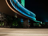 an illuminated pedestrian bridge is going over the street at night and passing by it at a curve