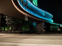 an illuminated pedestrian bridge is going over the street at night and passing by it at a curve