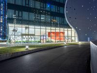 a long paved roadway leads to a glass building at night with many lights on it