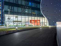 a long paved roadway leads to a glass building at night with many lights on it