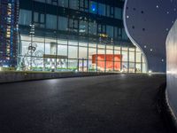 a long paved roadway leads to a glass building at night with many lights on it