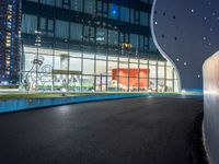 a long paved roadway leads to a glass building at night with many lights on it