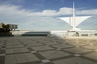 a white sculpture sitting in the middle of a tiled area under blue skies with a sky background