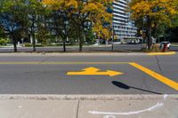 a yellow arrow painted on the side of a road near a sidewalk and traffic light