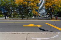 a yellow arrow painted on the side of a road near a sidewalk and traffic light