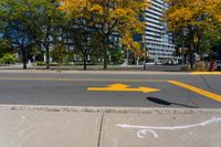 a yellow arrow painted on the side of a road near a sidewalk and traffic light