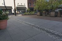 the sidewalk is empty near two planters with tables and chairs around it, and several people eating