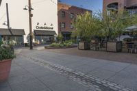 the sidewalk is empty near two planters with tables and chairs around it, and several people eating