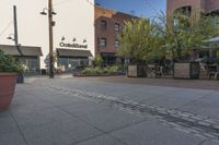 the sidewalk is empty near two planters with tables and chairs around it, and several people eating