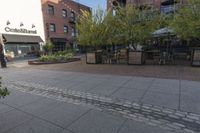 the sidewalk is empty near two planters with tables and chairs around it, and several people eating