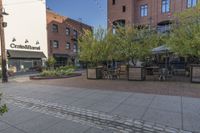 the sidewalk is empty near two planters with tables and chairs around it, and several people eating