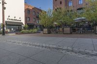 the sidewalk is empty near two planters with tables and chairs around it, and several people eating