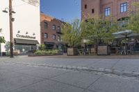 the sidewalk is empty near two planters with tables and chairs around it, and several people eating