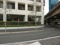 a red traffic light in the city by trees and bushes, some concretes and buildings and a red fire hydrant and sign