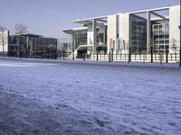 snow covering the ground and sidewalk of an industrial area with buildings, fences, and benches