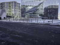 a paved area next to a big glass building with buildings on the left side of it