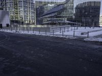 a paved area next to a big glass building with buildings on the left side of it