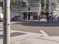 several people crossing an intersection in the city near tall buildings and palm trees, on a clear day