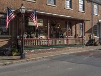 a couple of american flags outside of a building in a country town with some people walking