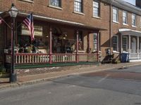 a couple of american flags outside of a building in a country town with some people walking