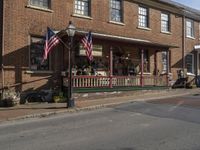 a couple of american flags outside of a building in a country town with some people walking