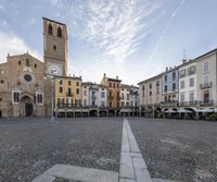 the square has many tables around it with chairs and umbrellas on the side and buildings in the distance