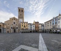 the square has many tables around it with chairs and umbrellas on the side and buildings in the distance