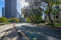 the sun is setting on an empty street that is filled with tall buildings and some trees