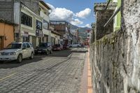 a very old looking street near some parked cars and buildings in a town area with some clouds in the sky