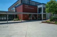 an entrance to the building has benches and trees around it on an asphalt surface with a blue sky in the background