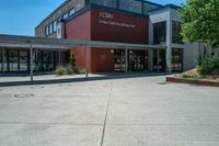 an entrance to the building has benches and trees around it on an asphalt surface with a blue sky in the background