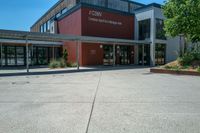 an entrance to the building has benches and trees around it on an asphalt surface with a blue sky in the background