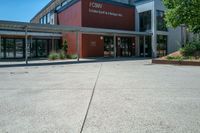 an entrance to the building has benches and trees around it on an asphalt surface with a blue sky in the background