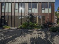 an outdoor building with lots of windows and plants on the side of the walkway near the front entrance