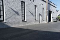 a concrete patio with windows, white brick wall, and cement walkway area next to it