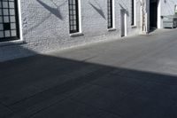 a concrete patio with windows, white brick wall, and cement walkway area next to it