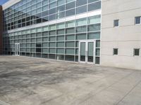 a bench outside an office building with large windows in the background / and a concrete grounding near the building