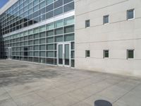 a bench outside an office building with large windows in the background / and a concrete grounding near the building