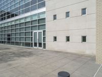 a bench outside an office building with large windows in the background / and a concrete grounding near the building