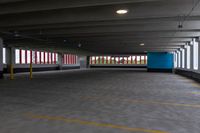 an empty parking garage with light posts in the distance and large windows in the background