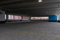 an empty parking garage with light posts in the distance and large windows in the background