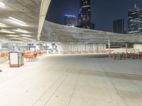 an empty parking garage with orange chairs at night time, in the city setting and empty tables on cement slabs