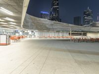 an empty parking garage with orange chairs at night time, in the city setting and empty tables on cement slabs