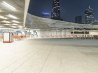 an empty parking garage with orange chairs at night time, in the city setting and empty tables on cement slabs