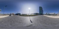 this is a fisheye image of an empty space with buildings in the background and a person skateboarding