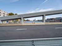 an overhead bridge that connects to an empty street and riverfront next to some city buildings