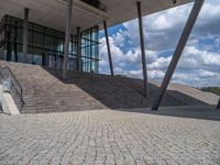 a person on a bike walking through a stone building entrance, in front of an enormous glass wall and stairs